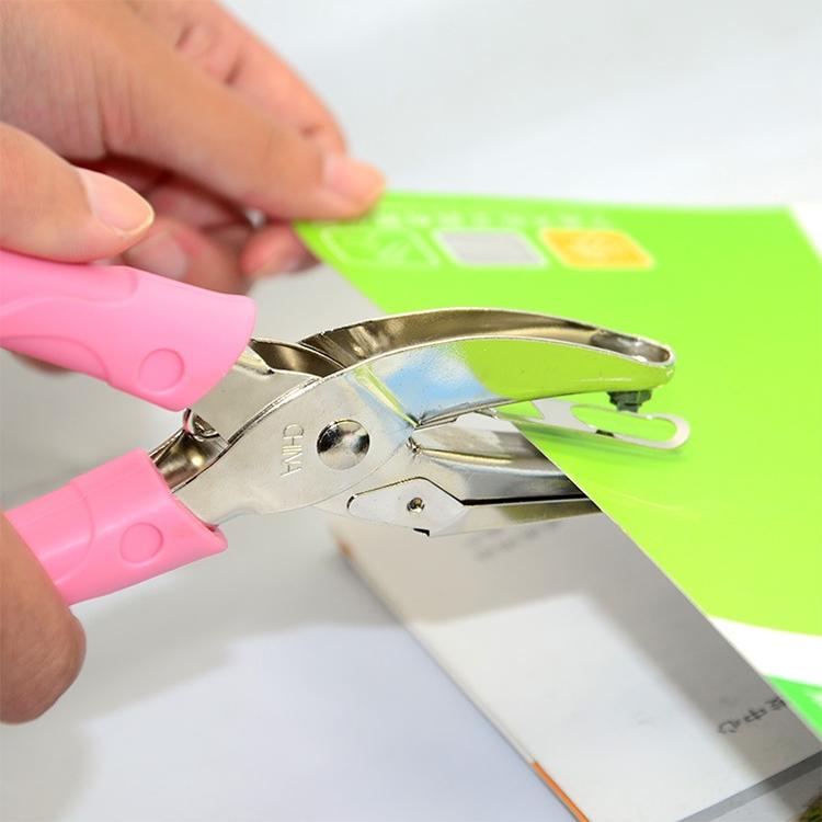 Manual hole punch applying punch to paper with pink handles and silver metal jaw