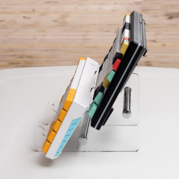 Transparent acrylic keyboard stand with metal pins, propped beside keycaps