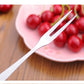 Single stainless steel fruit fork with prongs near cherries in a bowl