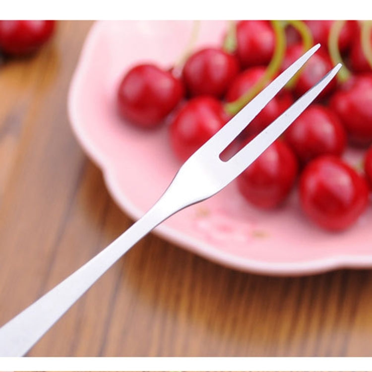 Single stainless steel fruit fork with prongs near cherries in a bowl