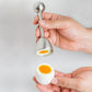Handheld stainless steel egg opener tool touching a whole egg