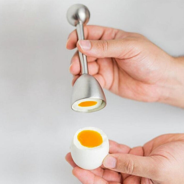 Handheld stainless steel egg opener tool touching a whole egg