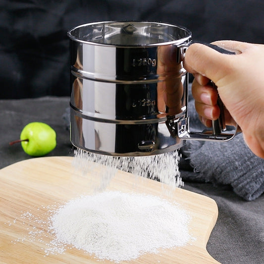 Stainless steel hand sifter with mesh bottom, handle and flour falling onto board