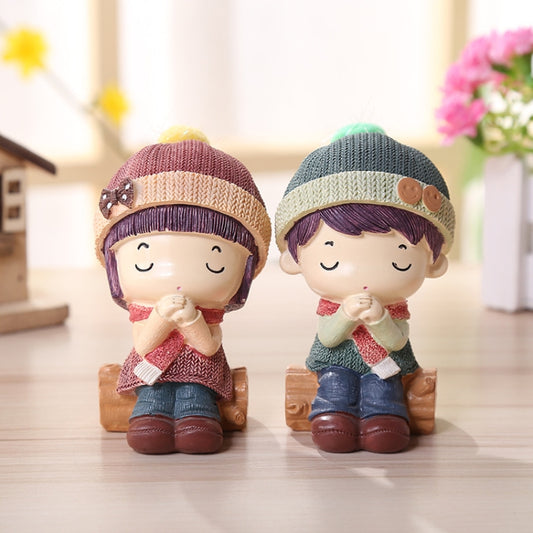 Resin doll figurines seated: one purple knit hat, one green knit hat, brown boots