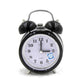 Black metal twin bell alarm clock with analog dial, quartz text, and blue night-light icon.