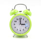 Green metal twin bell alarm clock with analog dial, quartz text, and blue night-light icon.