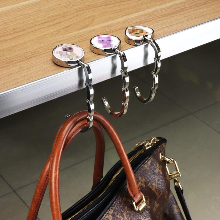 Chrome folding bag hanger with round disc top and hook clip holding a bag loop