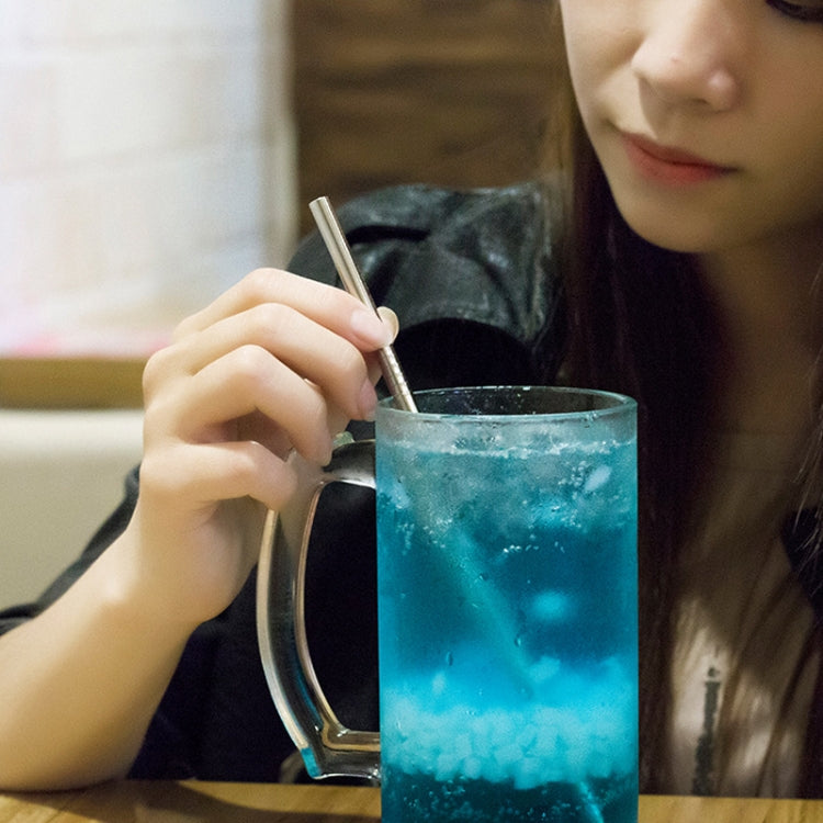 Reusable stainless steel drinking straw held above a glass, with straw brush set
