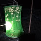 Green mesh hanging fly cage with trapped insects inside, illuminated at night