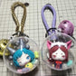 Clear plastic ball charm with cartoon doll inside, gold and purple braided loops
