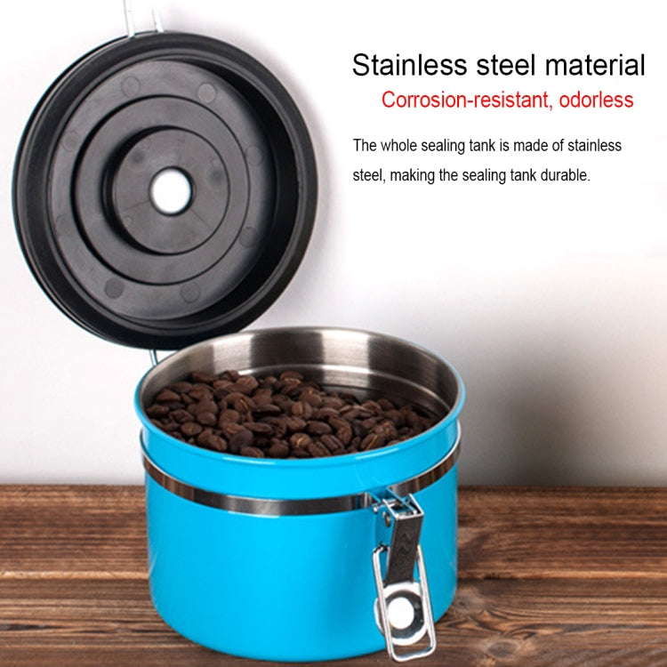 Stainless steel food storage container with black lid, latch, and coffee grounds inside.