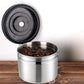 Stainless steel coffee storage container with open lid, latch, and coffee grounds.