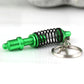 Green and black shock absorber keychain with silver key ring, angled view