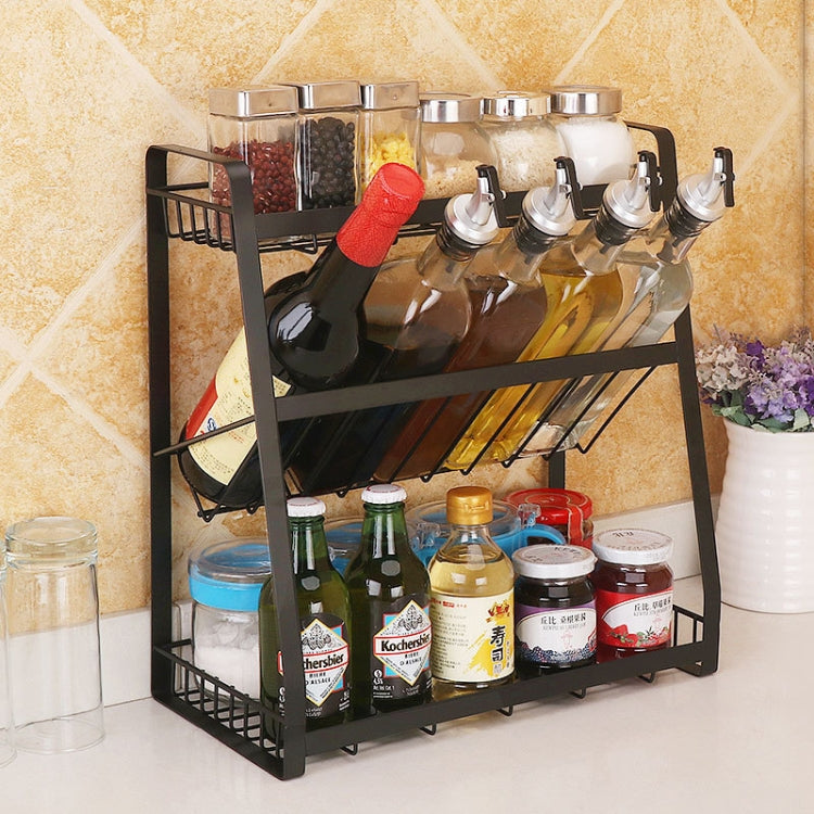 Black three-tier kitchen spice rack holding glass jars, bottles, and condiment tins