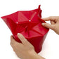 Red foldable silicone popcorn maker being unfolded by hands