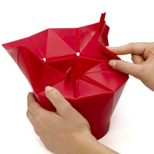 Red foldable silicone popcorn maker being unfolded by hands