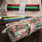 Close-up of canvas pencil roll: colorful pens, white elastic bands, rose-clock print lining