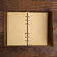 Loose-leaf travel diary notebook open to beige blank pages with metal ring spine