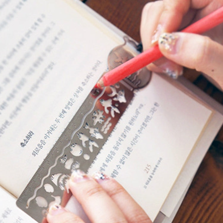 Gray metal bookmark ruler with cutout design, held on an open book page