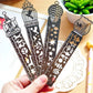 Five decorative metal bookmark rulers with cutout icons in hand over a book page