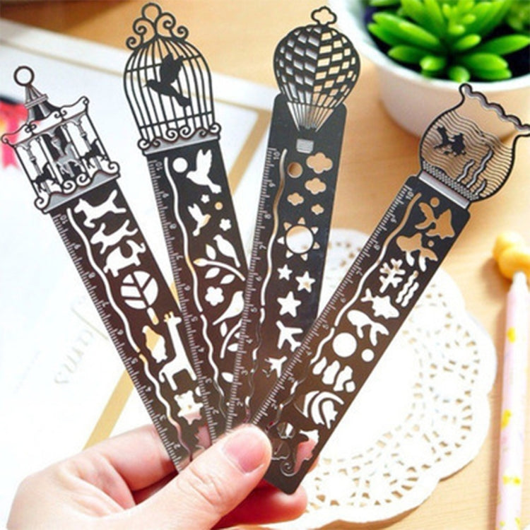 Five decorative metal bookmark rulers with cutout icons in hand over a book page