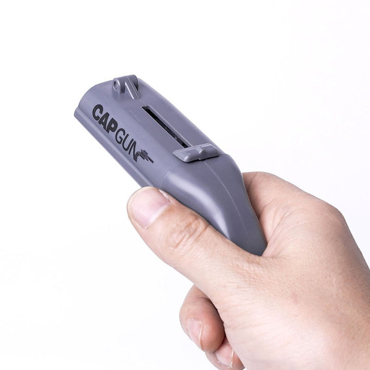 Grey cap gun bottle opener in hand, showing the top slot and CAPGUN branding.