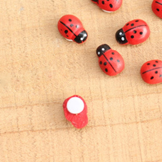 Red ladybug wooden cabochons with black spots and shiny silver backs, close-up on wood.