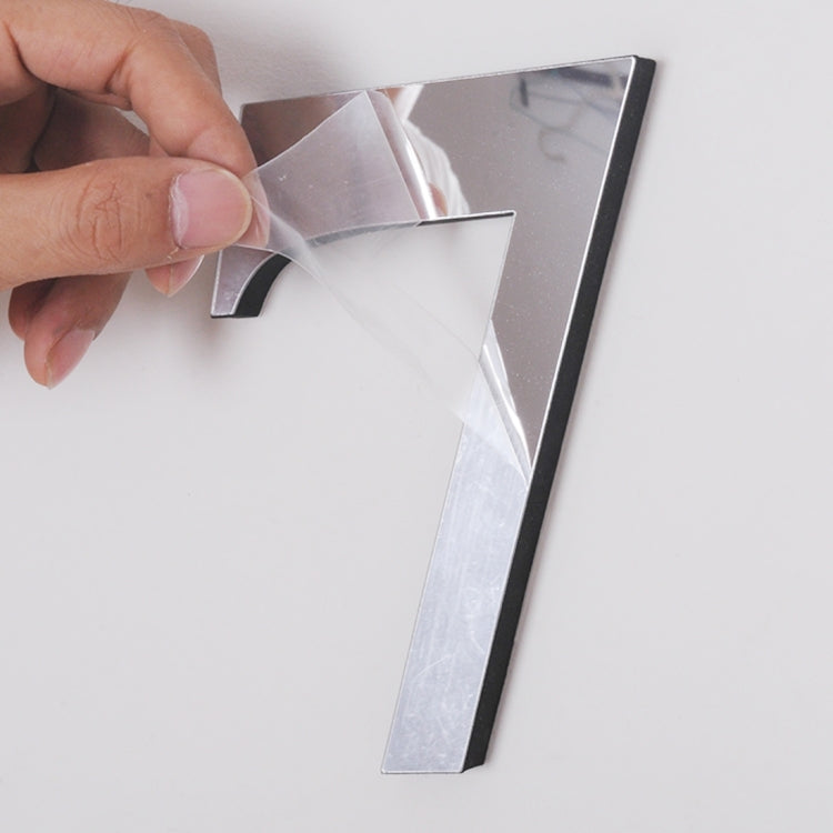 Hands aligning a reflective silver number sticker onto a wall