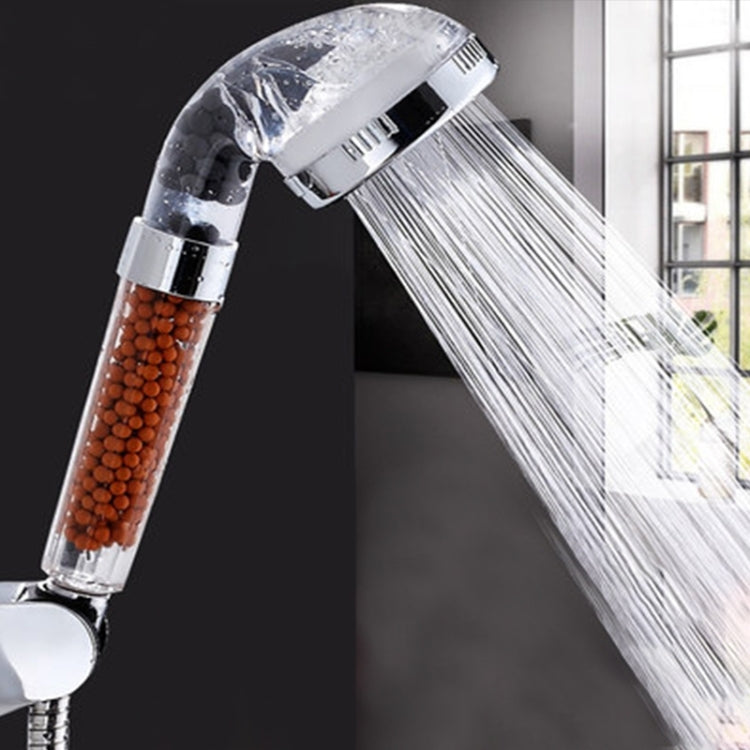Chrome shower head spraying water; translucent filter chamber with beads is visible