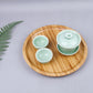 Round bamboo tea tray holding three green teacups with lids, 25 cm