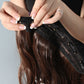 Clip-in hair extension being fastened with black comb clips onto dark brown hair