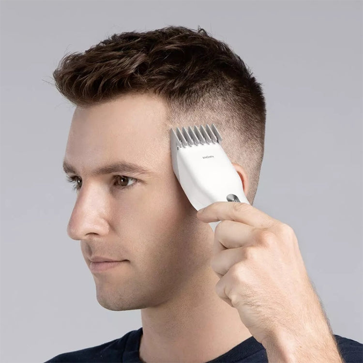 White electric hair trimmer trimming a man’s hair near the temple