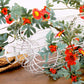 Close-up artificial flower vine with red-orange daisy blossoms and green leaves