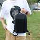 Black backpack worn crossbody-style with adjustable strap, front zipper pocket