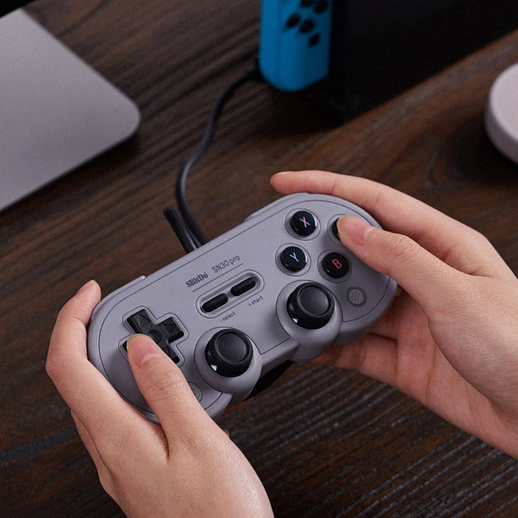 Grey wired gamepad held in hands with D-pad and analog sticks