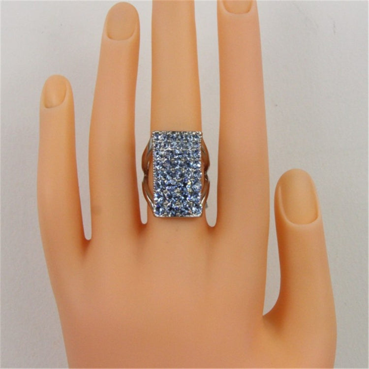 Blue crystal rectangular ring on finger, silver-tone openwork band
