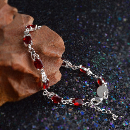 Silver bracelet with red oval ruby-like stones and linked chain.