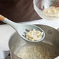 Gray silicone spoon ladle with wood handle lifting sliced onions from a pot