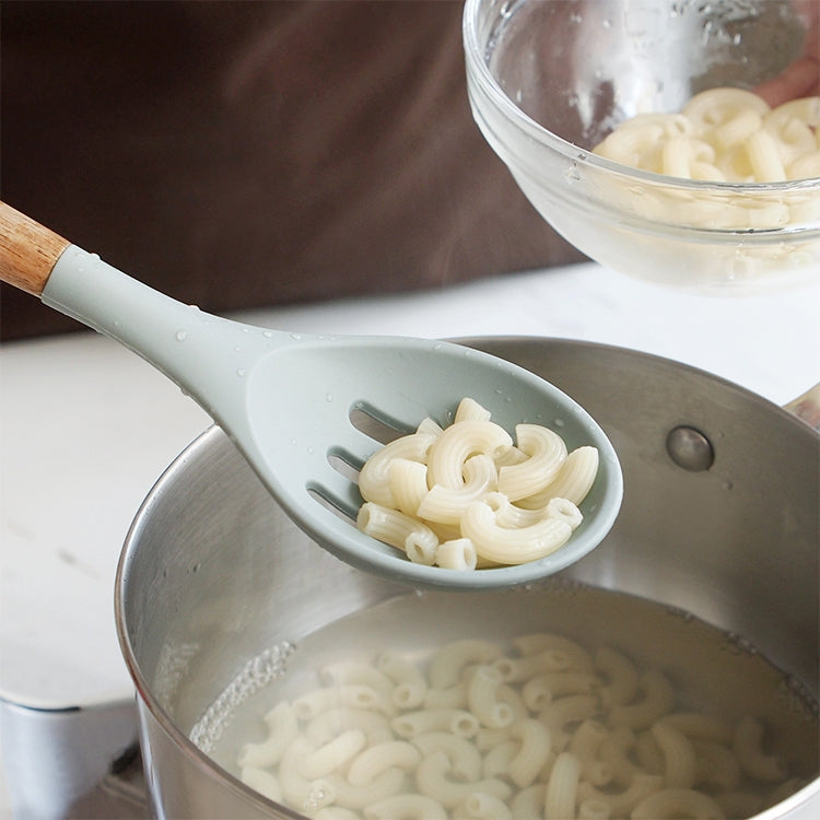 Gray silicone spoon ladle with wood handle lifting sliced onions from a pot