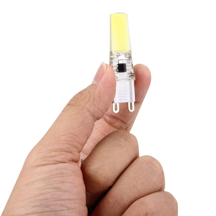 Dimmable LED plug bulb in hand, clear body with warm yellow light strip