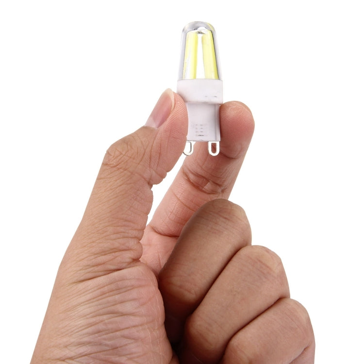 Hand holding a G9 dimmable LED bulb with clear glass and two-prong base