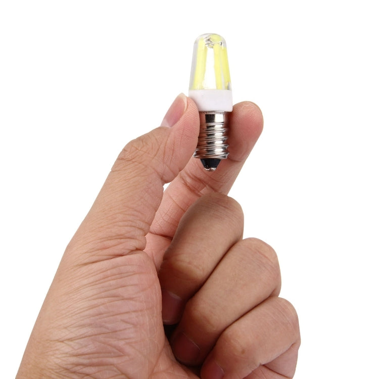 E14 LED bulb held in hand, clear glass with yellow filament, silver screw base