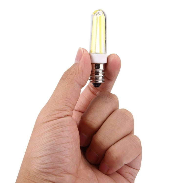 E14 LED bulb held in hand, clear glass tube with warm white filament glow