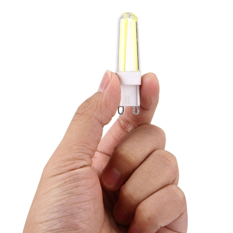 Hand holding a G9 dimmable LED lamp, clear tube with yellow glow and white base