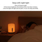 White bedside night light lamp emitting dim warm light beside a bed