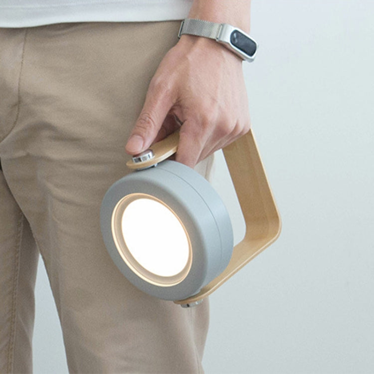 Portable white lantern lamp being held, circular light ring glowing with wood handle