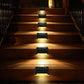 Black solar step lights glowing warm on an outdoor wooden staircase at night.