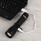 Black USB charging LED torch flashlight connected to white cable near keyboard
