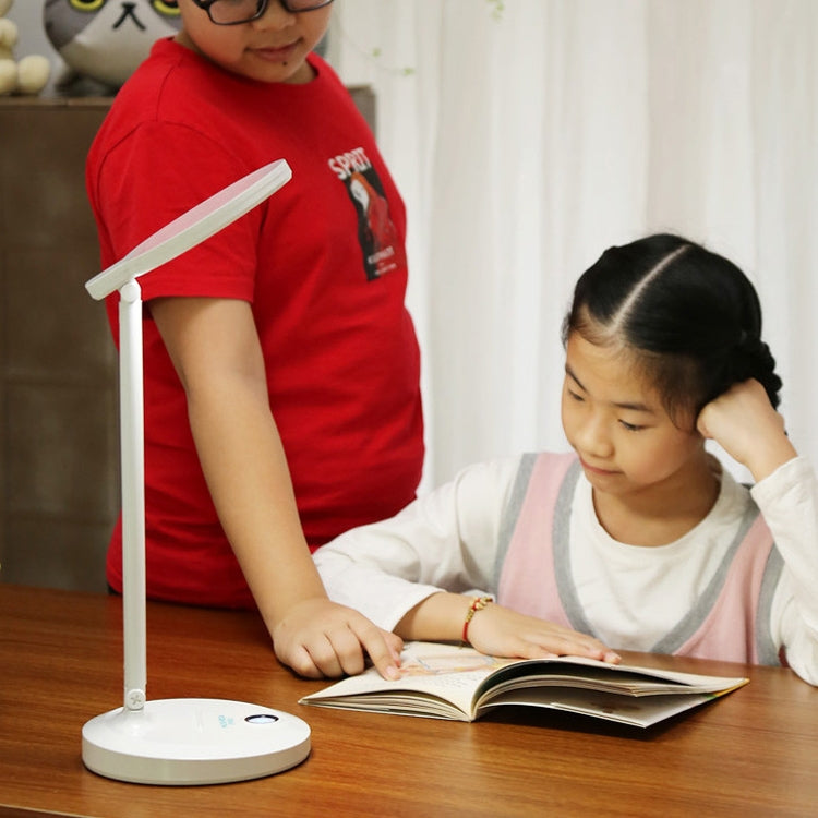 White foldable LED desk lamp illuminating an open book on a desk