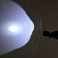 Compact flashlight projecting a bright circular beam; black body with blue button.